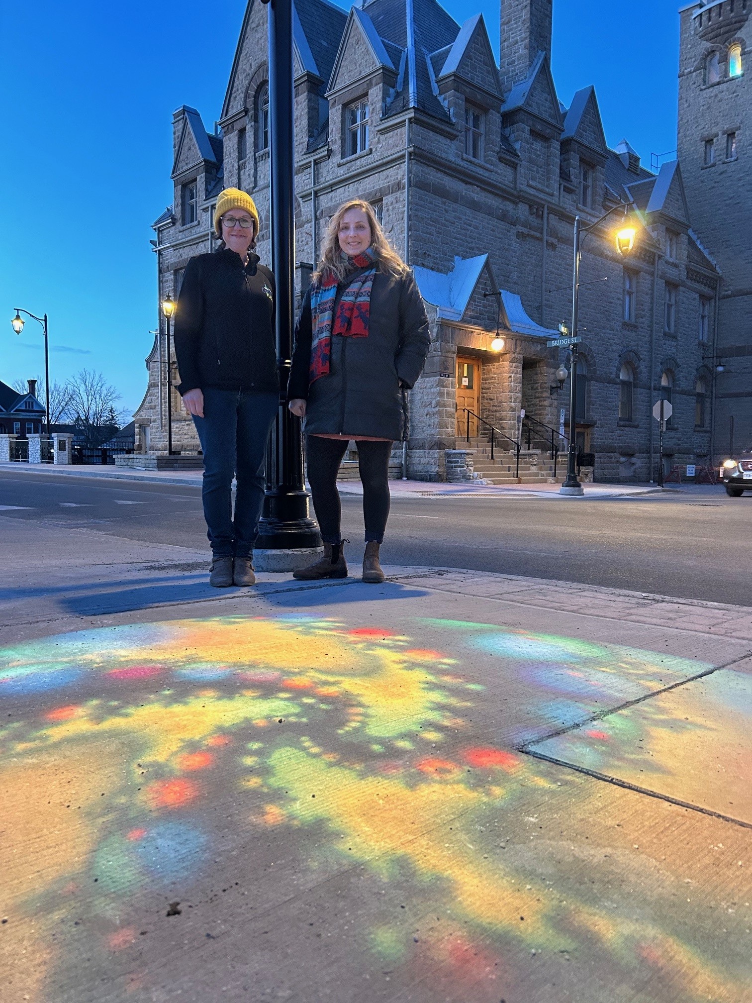 two women standing in front of light street art
