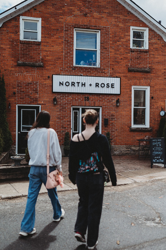 two women walking towards a red brick building with a sign that says North + Rose